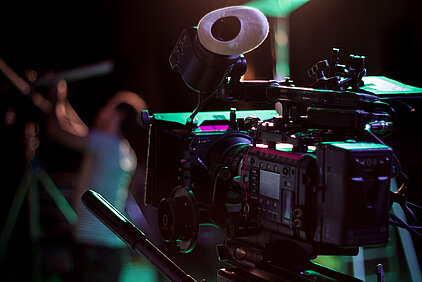 devant une camera de cinéma un électricien règle un projecteur éclairant la scène qui va être tournée